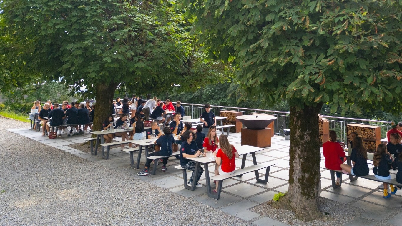 A group of students enjoy their meals at an outdoor eating area surrounded with trees. A group of students enjoy their meals at an outdoor eating area surrounded with trees.