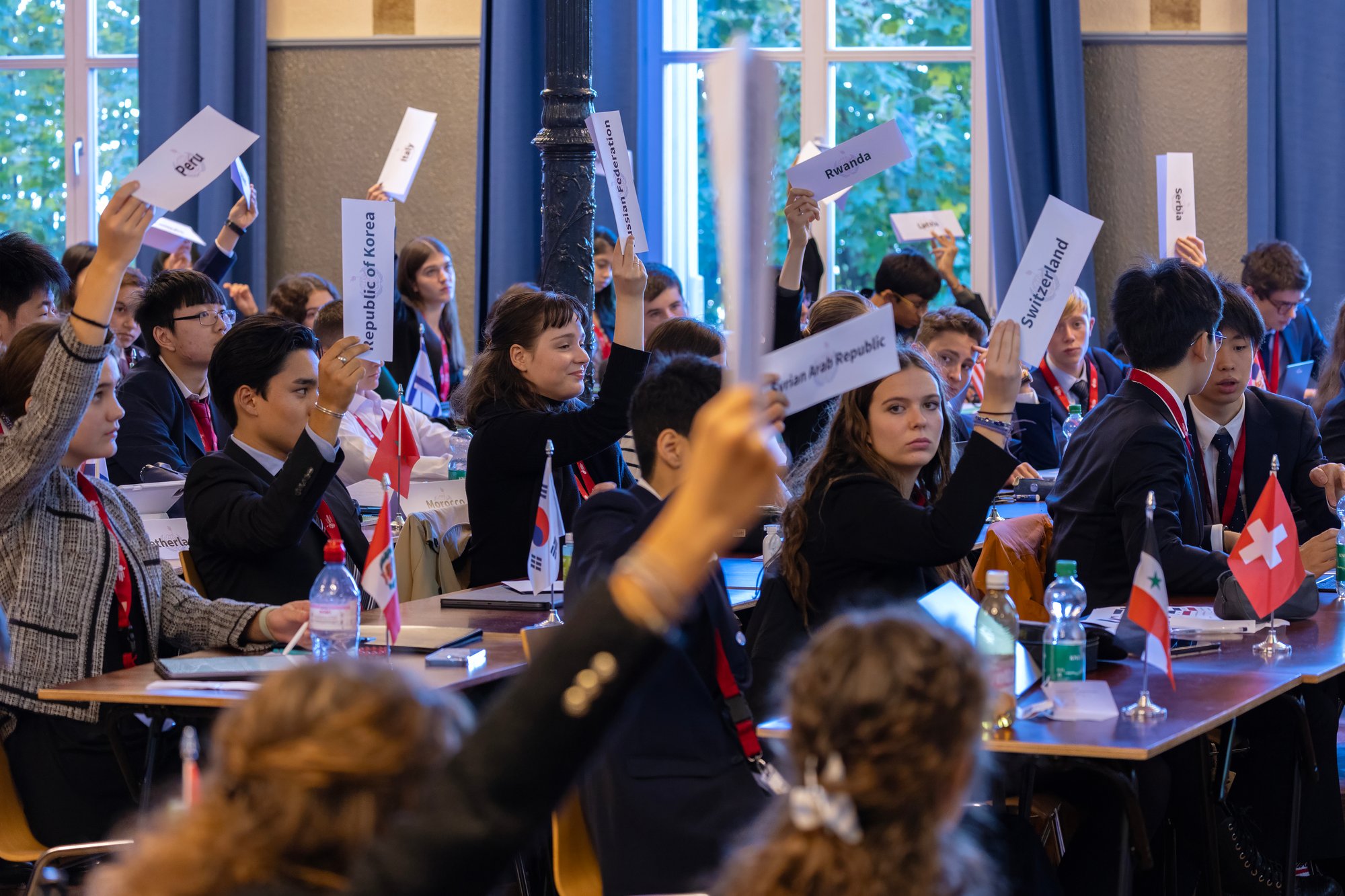 A group of students in the middle of a conference, most of them hold a paper showing their country origin. A group of students in the middle of a conference, most of them hold a paper showing their country origin.