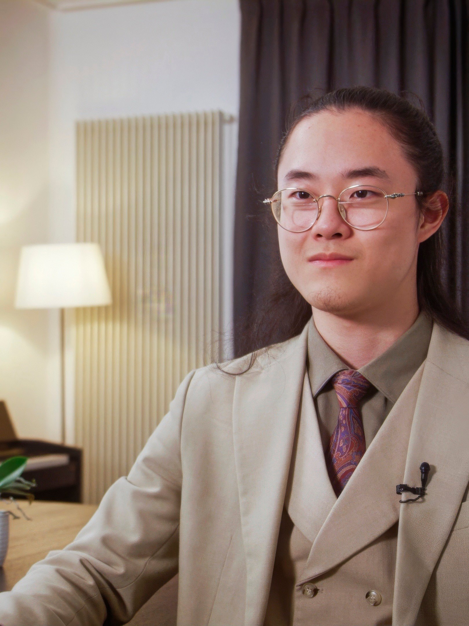 A young asian man in glasses and cream suit.